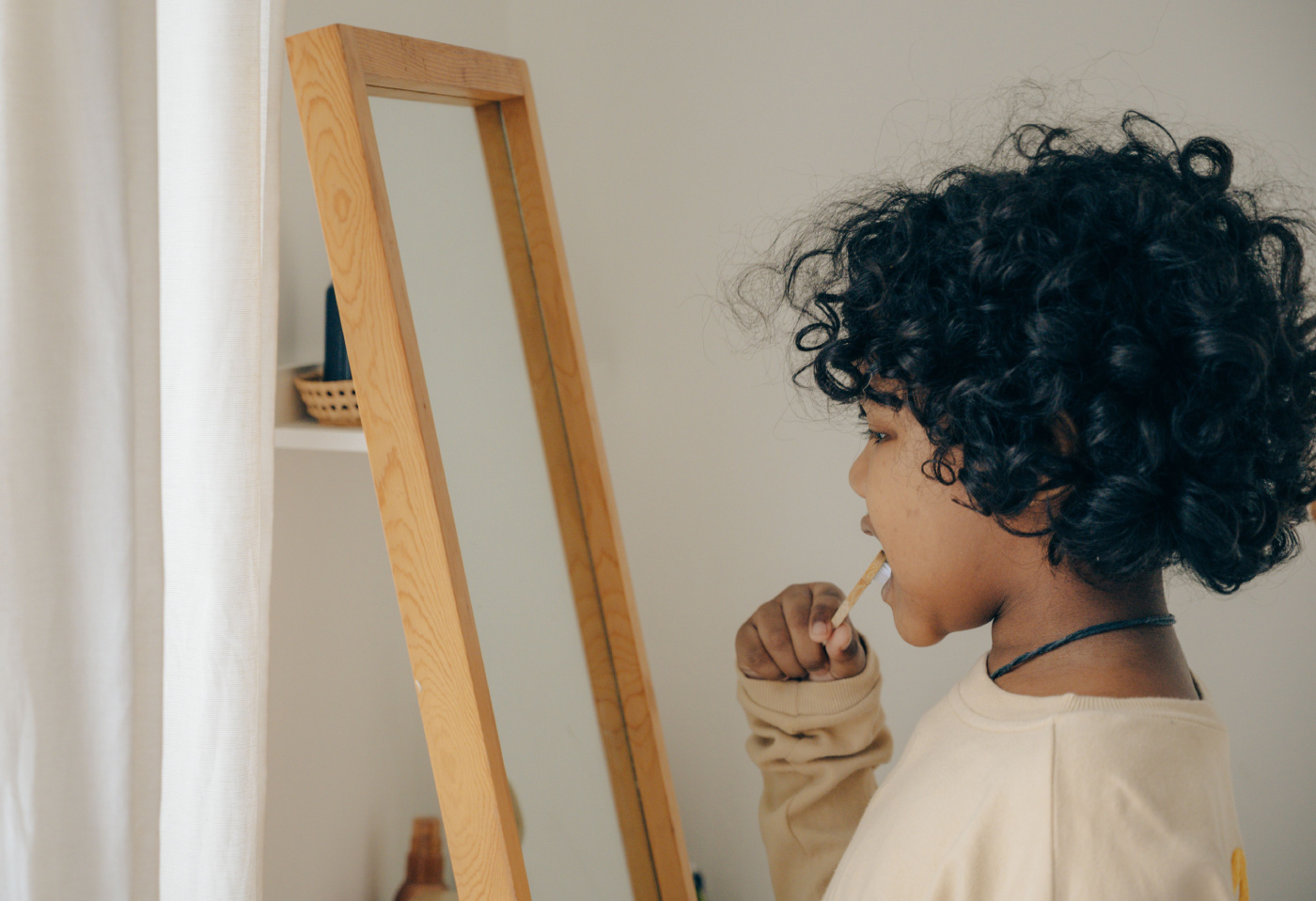 A curly black hair child looking into a wooden-framed mirror in a softly lit room, creating a calm mood.